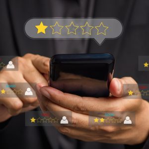 A person holding their phone and scrolling with their finger. Digital graphics around the phone display low reviews.