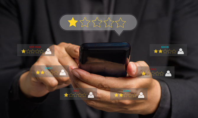 A person holding their phone and scrolling with their finger. Digital graphics around the phone display low reviews.