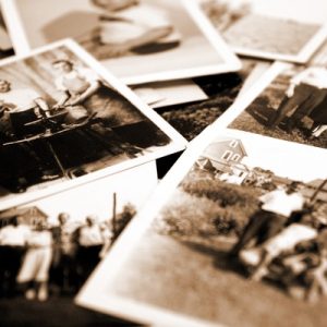 A close up of multiple old photographs sitting on a table. The photos are black and white and sepia.
