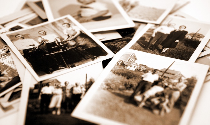 A close up of multiple old photographs sitting on a table. The photos are black and white and sepia.