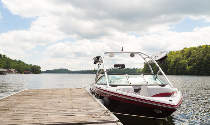 A personal speed boat parked near a small wooden dock on a sunny day. The boat has a wakeboard rack near the front.
