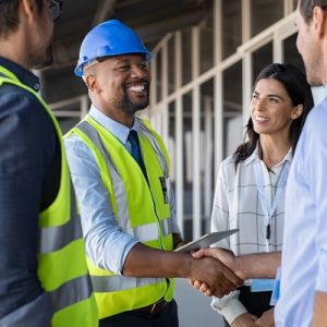 Contractors wearing safety vests and helmets on a construction site, with one giving a man a handshake next to a woman.