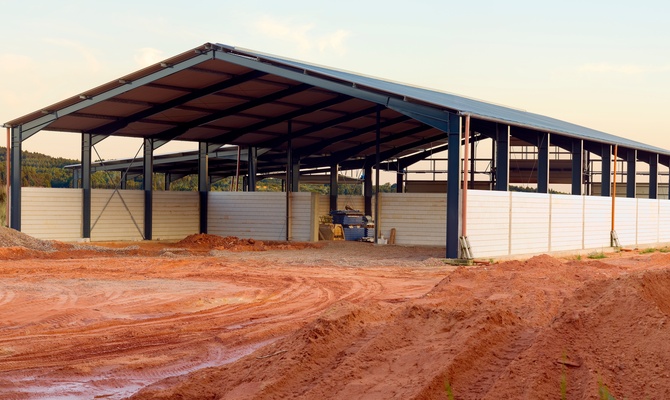 A pole barn with white siding and a peaked metal roof undergoing construction near a large dirt clearing.