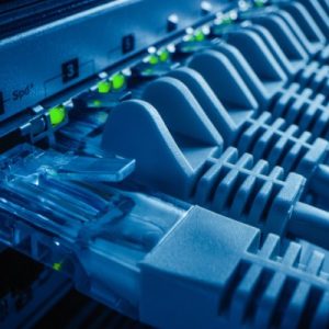 A close-up view shows a hand plugging a blue data cable into a port next to other blue cables. Green lights are glowing.