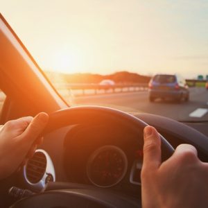 A close-up of a driver's hands on the steering wheel. He's driving on a stretch of highway.