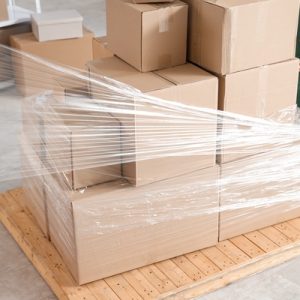 Two warehouse workers wrapping a loaded pallet in stretch film. One is unrolling the film while the other stabilizes the boxes.