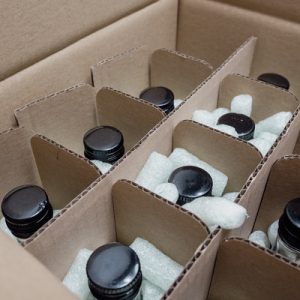 A cardboard box contains a four-by-three cardboard grid. Each compartment contains a bottle with a black top.