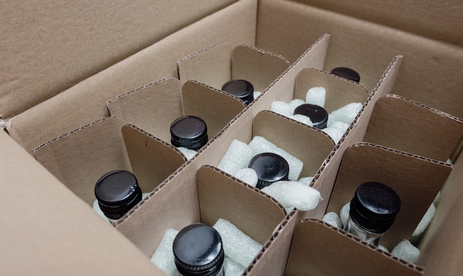 A cardboard box contains a four-by-three cardboard grid. Each compartment contains a bottle with a black top.