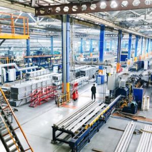 A manufacturing warehouse with newer industrial equipment and bright lighting. One person stands in the middle of it all.