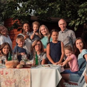 A photographer kneels down and takes a photo of a large family of children and older adults around a table.
