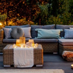 Home outdoor living space with a teak sectional couch with gray cushions and a teak table with multiple candles on top.