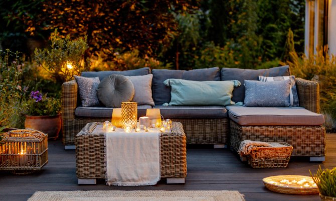 Home outdoor living space with a teak sectional couch with gray cushions and a teak table with multiple candles on top.