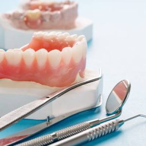 A close-up of top dentures with dental repair tools nearby and more incomplete dentures in the background.