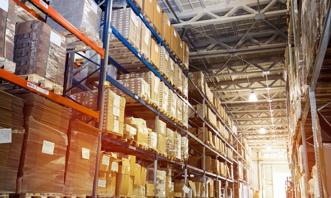 The inside of a warehouse with a long hallway lined with shelving units that hold products for the facility.