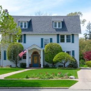 The exterior of a multistory colonial-style house with white siding, blue shutters, and a well-manicured front lawn.