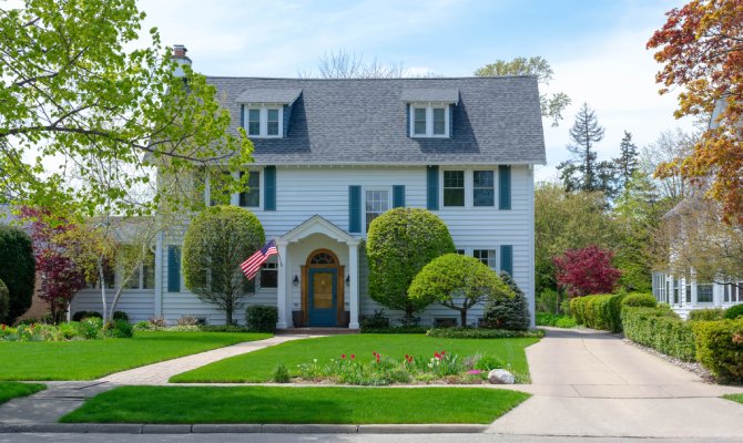 The exterior of a multistory colonial-style house with white siding, blue shutters, and a well-manicured front lawn.