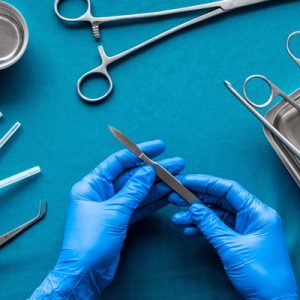 A surgeon prepares for plastic surgery, holding a scalpel on a blue surgical table with other tools.