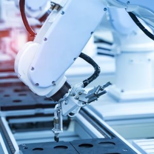 A close-up view of a white robotic arm surrounded by other robotics as it operates on a production line.