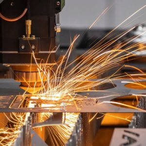 A cutting machine cutting out shapes and designs in a thin piece of sheet metal. Sparks fly from the metal.