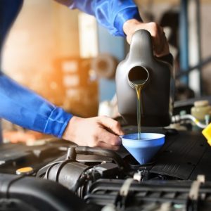 A close-up of a mechanic's hand refilling car oil in a service center. They're wearing a blue uniform.