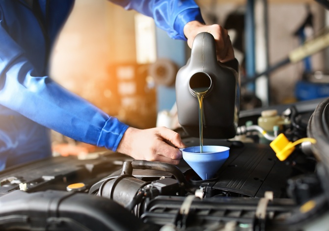 A close-up of a mechanic's hand refilling car oil in a service center. They're wearing a blue uniform.