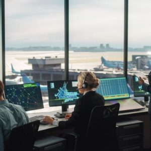Four air traffic controllers monitoring computer screens in a control tower with curved glass walls.