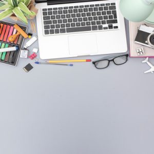 An overview of a desk that's full of creative supplies and tools, like a camera, markers, pencils, and a MacBook.
