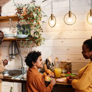A man, a woman, and a young boy cook together in a rustic kitchen featuring shiplap walls and wooden shelves.
