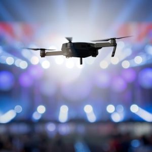 A drone flies above a concert, recording the event as bright stage lights shine out toward the audience.