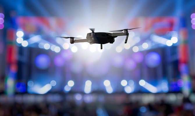 A drone flies above a concert, recording the event as bright stage lights shine out toward the audience.
