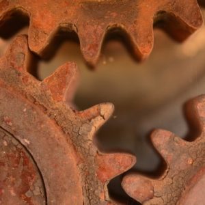 A close-up view of three interlocked gears. Each of them is heavily rusted and starting to break apart.