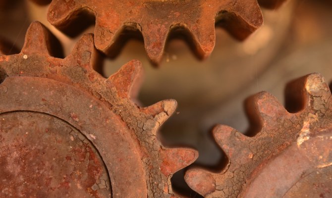 A close-up view of three interlocked gears. Each of them is heavily rusted and starting to break apart.