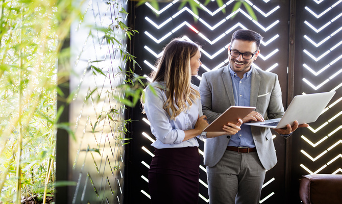 Two business colleagues at a meeting in a modern office interior with greenery hanging from the ceiling.