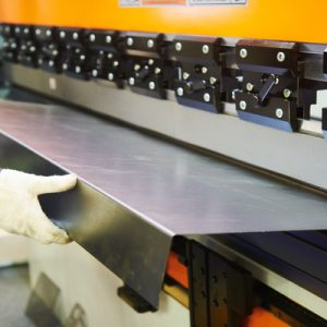 A close-up of a professional engineer using a hydraulic press brake or bending machine for flat sheet metal.