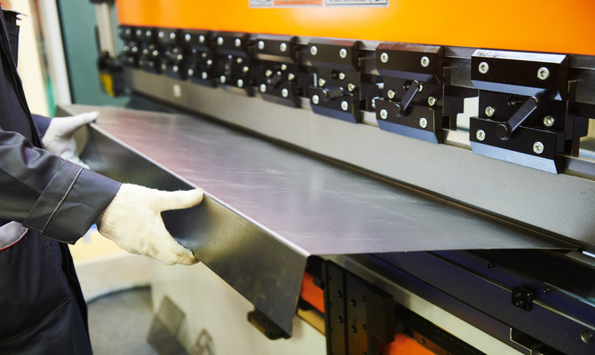 A close-up of a professional engineer using a hydraulic press brake or bending machine for flat sheet metal.