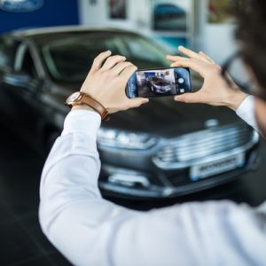 An over-the-shoulder view of someone taking a photo of their black vehicle using their smartphone camera.