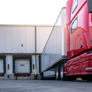 A red semi-truck pulled into a transportation dock where several trailers are lined up in their bays.