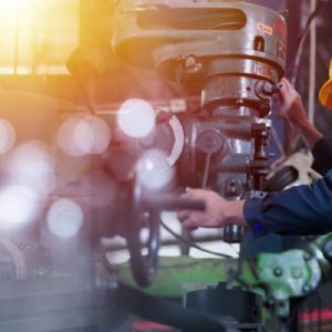 A male professional engineer wears a hard hat and safety glasses while operating machinery in a factory.