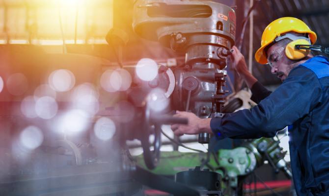A male professional engineer wears a hard hat and safety glasses while operating machinery in a factory.
