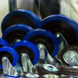 A close-up of various blue and black caster wheels arranged on a reflective surface in a bright setting.