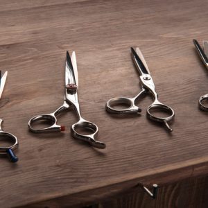 Four sets of haircutting shears, all sitting on a wooden counter. Each of them is slightly different from each other.
