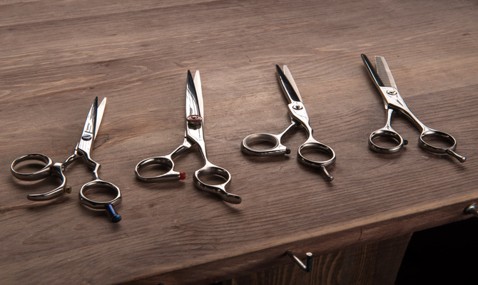 Four sets of haircutting shears, all sitting on a wooden counter. Each of them is slightly different from each other.