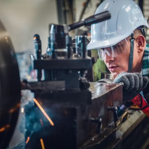 A close-up of a Caucasian male mechanical engineer working on a lathe machine in a metalwork factory.