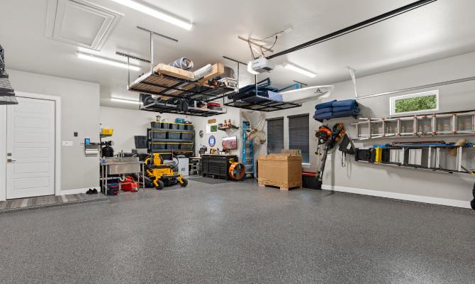 An organized residential garage has overhead storage with bins, a tool organization system, and ladders hanging on the wall.