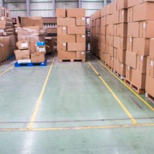 A section of a warehouse, cordoned off with yellow tape, for pallets with tall stacks of cardboard boxes.