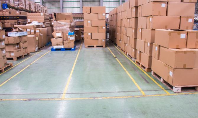 A section of a warehouse, cordoned off with yellow tape, for pallets with tall stacks of cardboard boxes.
