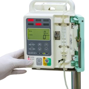 The close-up view shows a person wearing a white latex glove pushing the button on an infusion pump.