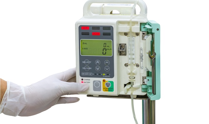 The close-up view shows a person wearing a white latex glove pushing the button on an infusion pump.