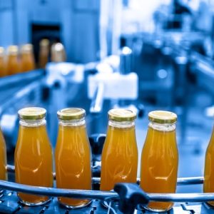 Glass bottles filled with orange juice move along a curved conveyor line in a blue-toned industrial bottling facility.