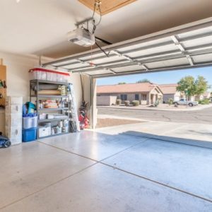 A home's garage door is wide open, revealing the surrounding neighborhood outside. Its walls feature shelves.
